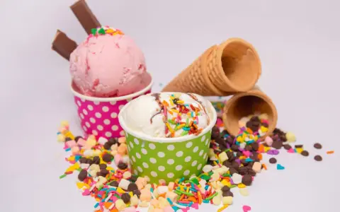 Zwei Becher mit Eiscreme, einer rosa, der andere weiß, bestreut mit bunten Streuseln und Schokostückchen. So sieht leckeres Gelato aus!