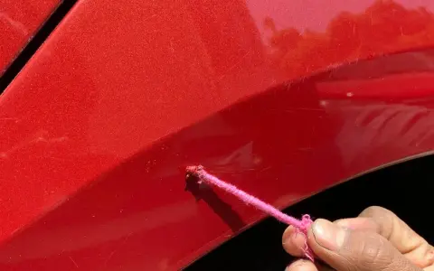 Różowa nitka z farbą na czerwonym lakierze auta, próba zrobienia zaprawki.