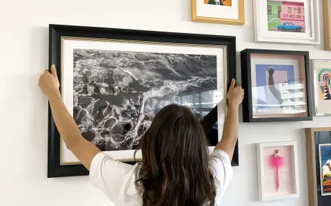 Une femme ajuste un grand cadre noir avec une photo d'eau en noir et blanc. Elle est en train de fabriquer un cadre pour sa maison.
