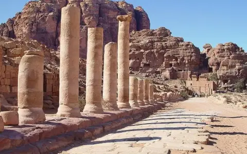 Columnas antiguas en Petra, una de las 7 maravillas del mundo, flanquean un camino de piedra bajo un cielo azul.