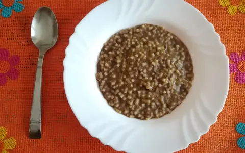 Piatto di pasta e lenticchie fumante, pronto per essere gustato. Un cucchiaio d'argento attende accanto.