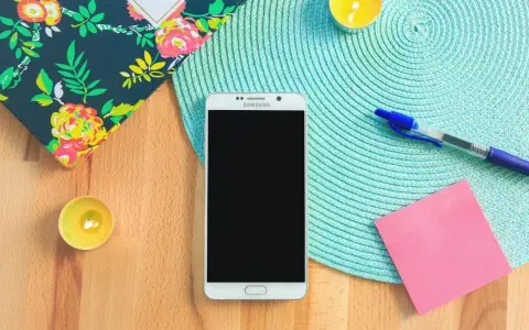 Un smartphone prêt à vous aider à vous organiser au quotidien. Un carnet fleuri, des bougies, un stylo et un post-it rose complètent la scène.