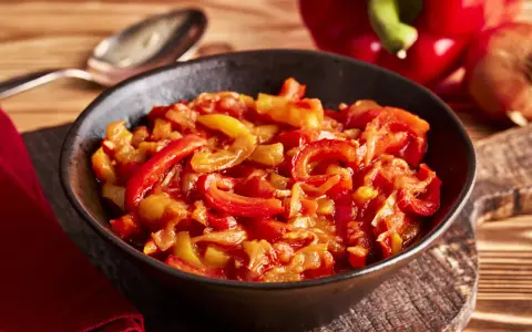 Schmor paprika mit Zwiebeln, ein Gericht, das man gut letscho selber machen kann. Serviert in einer Schüssel auf einem Holztisch.
