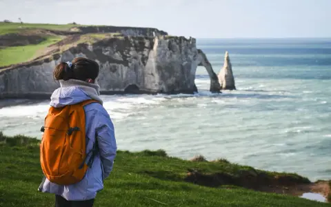 Une randonneuse admire les falaises d'Étretat, un paysage spectaculaire rappelant la beauté sauvage de la baie de Somme.
