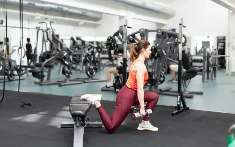 Kvinna utför bulgarian split squat med hantlar på gym.