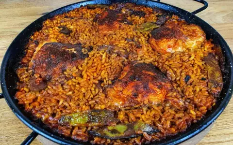 Pyszna paella z kurczakiem, ryżem i warzywami w tradycyjnej patelni.