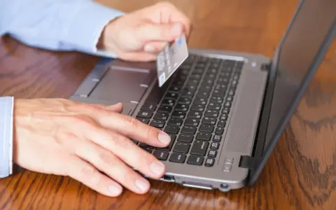 Mężczyzna z kartą płatniczą przy laptopie, szuka informacji jak sprawdzić blokady na koncie PeoPay.