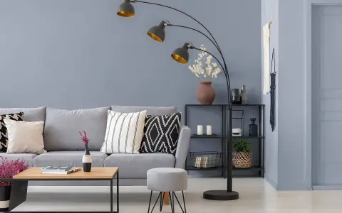 Sofa w odcieniu **szarym** i **grafitowym** z poduszkami, obok stolik i pufka. W tle regał z dekoracjami.