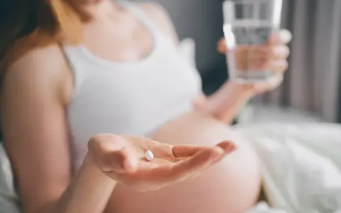 Ciężarna kobieta bierze tabletkę, by złagodzić objawy anginy. Dba o zdrowie swoje i dziecka.