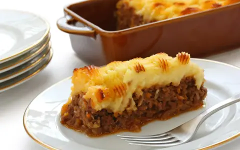 Une part de hachis parmentier, prêt pour la cuisson chaleur tournante, sur une assiette blanche.