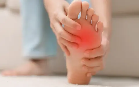 Persona se toca la almohadilla del pie, con una zona roja indicando dolor. Busca remedios caseros para el dolor en la almohadilla del pie.