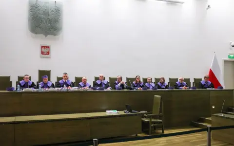 Sędziowie w togach siedzą za stołem w sali sądowej, przygotowując się do rozprawy przed trybunałem stanu.