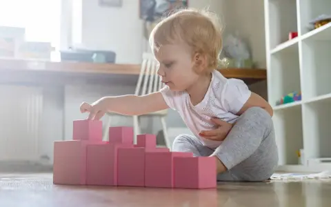 Bambina bionda gioca con blocchi rosa, ideali come giochi montessori 6 mesi fai da te per sviluppare la coordinazione.