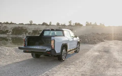 Biały maxus pickup z otwartą paką stoi na żwirowej drodze przy zbiorniku wodnym.