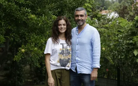La forza di una donna puntata di oggi: una coppia sorride tra gli alberi. Lei indossa una maglietta con una bomba floreale, lui una camicia azzurra.