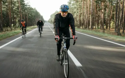 Cyclists on a road through a forest, likely engaged in a VO2 max training program, pushing their limits.