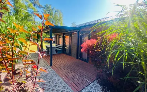 Uroczy tiny house wynajem. Drewniany domek z tarasem, otoczony zielenią i kwitnącymi krzewami. Idealne miejsce na relaks.
