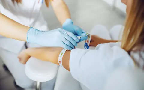 Pielęgniarka w rękawiczkach zakłada opaskę uciskową przed pobraniem krwi. Dowiedz się, gdzie zrobić badania krwi na NFZ.