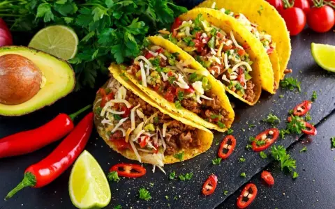 Pyszne dania meksykańskie: tacos z mielonym mięsem, serem, pomidorami i awokado, ozdobione papryczkami chili i limonką.