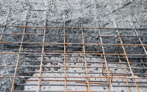 Zbrojenie fundamentów z betonu. Siatka z prętów stalowych pokryta świeżą masą betonową, gotowa do utwardzenia.