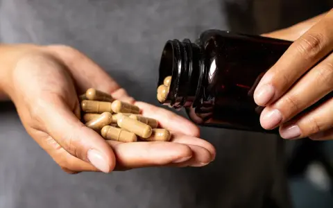 Hände schütten Kapseln aus einer braunen Flasche. Die Kapseln liegen in der Handfläche, bereit zur Einnahme. Möglicherweise zur Unterstützung der chrom wirkung.