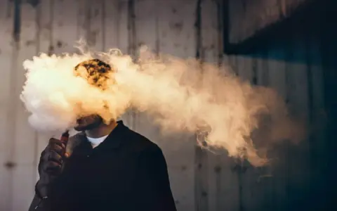 Hombre exhalando una gran nube de humo vaper, que envuelve su cabeza.