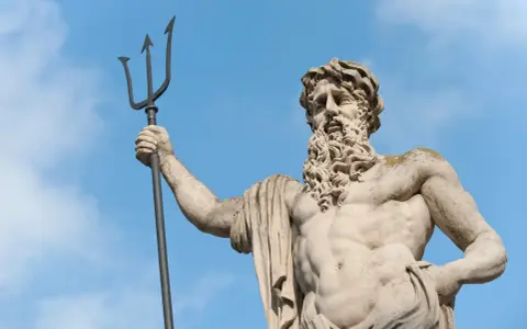 Statue de Poseidon dieu des mers, tenant son trident, sous un ciel bleu.