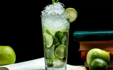 Orzeźwiający mojito przepis: szklanka pełna lodu, mięty i limonki, obok jabłka i książki. Idealny na letnie popołudnie.