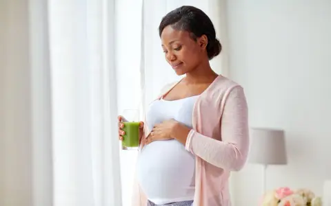 Femme enceinte tenant un verre de jus vert, caressant son ventre. Elle prend soin de sa peau sèche pendant la grossesse.