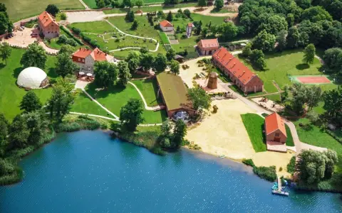 Widok z lotu ptaka na ośrodek SPA nad jeziorem z budynkami, plażą i kortem tenisowym.