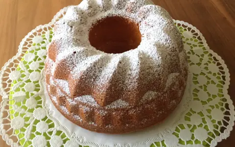 Ein goldbrauner Quark Gugelhupf, bestäubt mit Puderzucker, auf einer zarten Spitzendeckchen.
