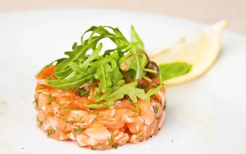 Un délicieux tartare de saumon frais, garni de roquette et d'une tranche de citron, prêt à être dégusté.