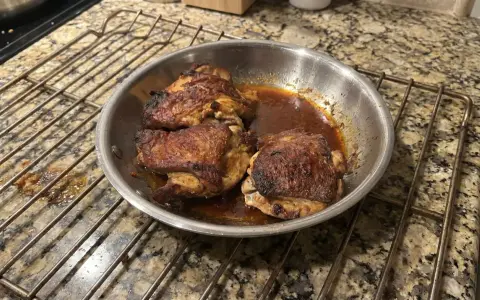Succulente cosce di pollo in padella, dorate e saporite, riposano su una griglia.