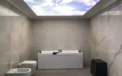 Bagno moderno con vasca, bidet e WC. Il soffitto in cartongesso riproduce un cielo azzurro con nuvole, creando un'atmosfera rilassante.