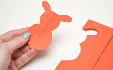 En hand håller en orange pappersfigur av en påskhare.