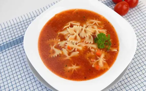 Zupa pomidorowa z makaronem farfalle, marchewką i natką pietruszki na kratkowanym obrusie.