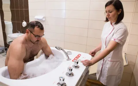 Mężczyzna w wannie z pianą, terapeuta przygotowuje masaż wirowy kończyn dolnych.