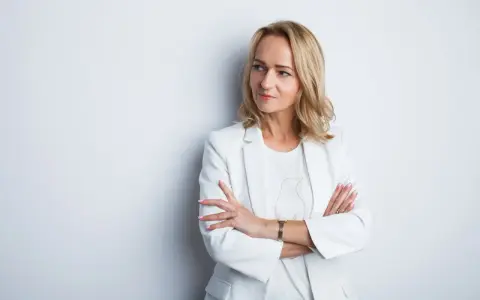 Elegancka kobieta w białej marynarce, z rękami skrzyżowanymi na piersi. Idealne zdjęcie do CV, podkreślające profesjonalizm i pewność siebie.