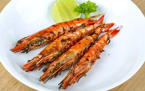 Cuatro langostinos a la plancha, dorados y jugosos, servidos en plato blanco con rodaja de limón y perejil.