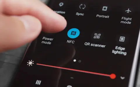 En finger pekar på NFC-ikonen på en mobilskärm. Snabbinställningar visas, inklusive "Power mode" och "QR scanner".