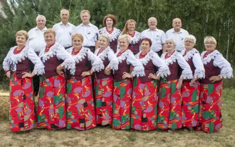 Grupa ludzi w strojach ludowych, kobiety w czerwonych korale i wzorzystych spódnicach, mężczyźni w białych koszulach. Kto śpiewa czerwona jarzębina?