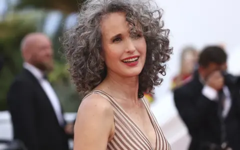 Mujer sonríe con modernos cortes de pelo con canas, luciendo un vestido a rayas.
