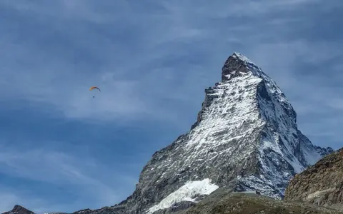 Widok na ośnieżony szczyt Matterhornu, z paralotnią szybującą na błękitnym niebie. To jak wejście na Mont Blanc dla odważnych.