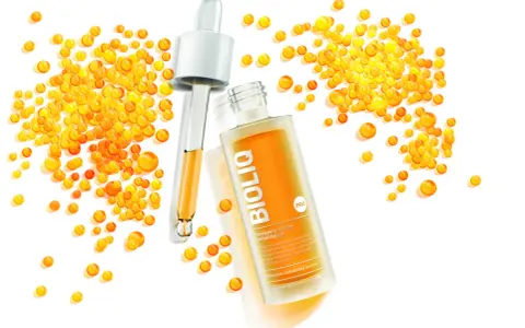 BiolIQ intensywne serum rewitalizujące w buteleczce z pipetą, otoczone kropelkami o pomarańczowym odcieniu.