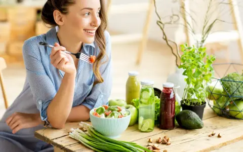 Kvinna äter sallad, omgiven av hälsosam mat. Kan vara en del av en kost för att undvika brist på kisel symtom.