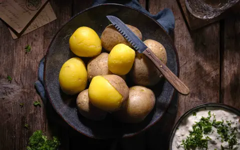 Gekochte und rohe Kartoffeln liegen in einer Schale, bereit für ein deftiges Essen. Ein Messer mit Holzgriff liegt daneben.