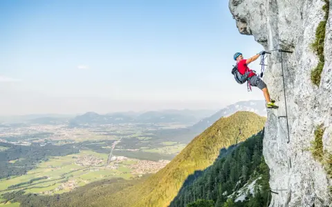 Ein Mann klettert gesichert an einem Stahlseil einen Felsgrat entlang. Ein Abenteuer auf einem der vielen Klettersteige Deutschlands.