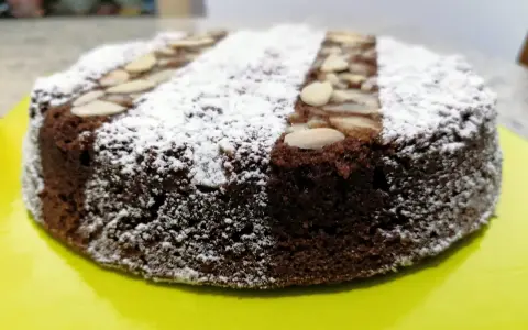 Torta caprese ricetta originale napoletana, soffice e scura, cosparsa di zucchero a velo e mandorle a lamelle.