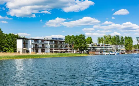 Nowoczesny Tiffi Hotel Olsztyn nad jeziorem, z łodziami przy pomoście i zielenią.