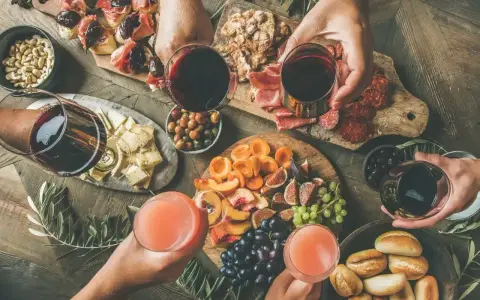 Stół z przekąskami: wędliny, sery, owoce, pieczywo i napoje.